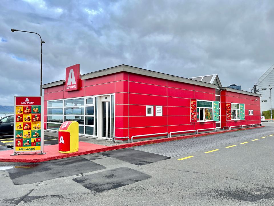 A bright red fast food building with drive-thru menu signs outdoors.