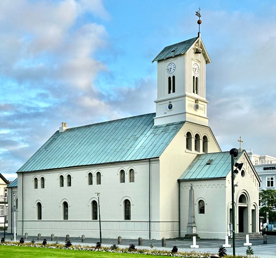 Exterior view of a white historic cathedral with a wooden clock tower in Reykjavík