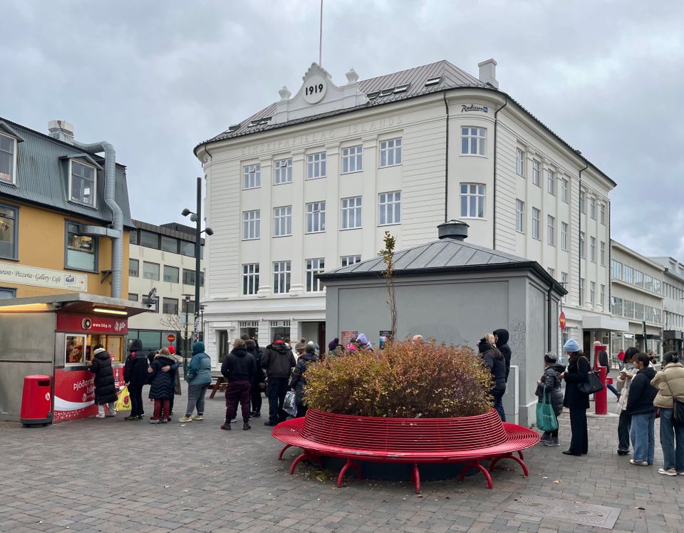 A group of people queuing near a small street food kiosk in a public square.