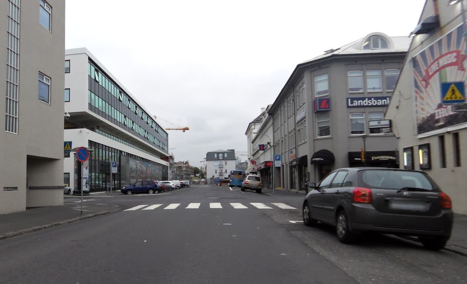A paved city street in Reykjavik with parked cars and commercial buildings under an overcast sky.