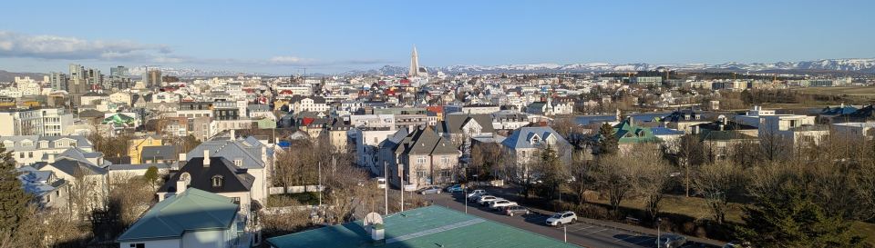 A wide panoramic view of the Reykjavik cityscape with mountains in the background under a clear sky