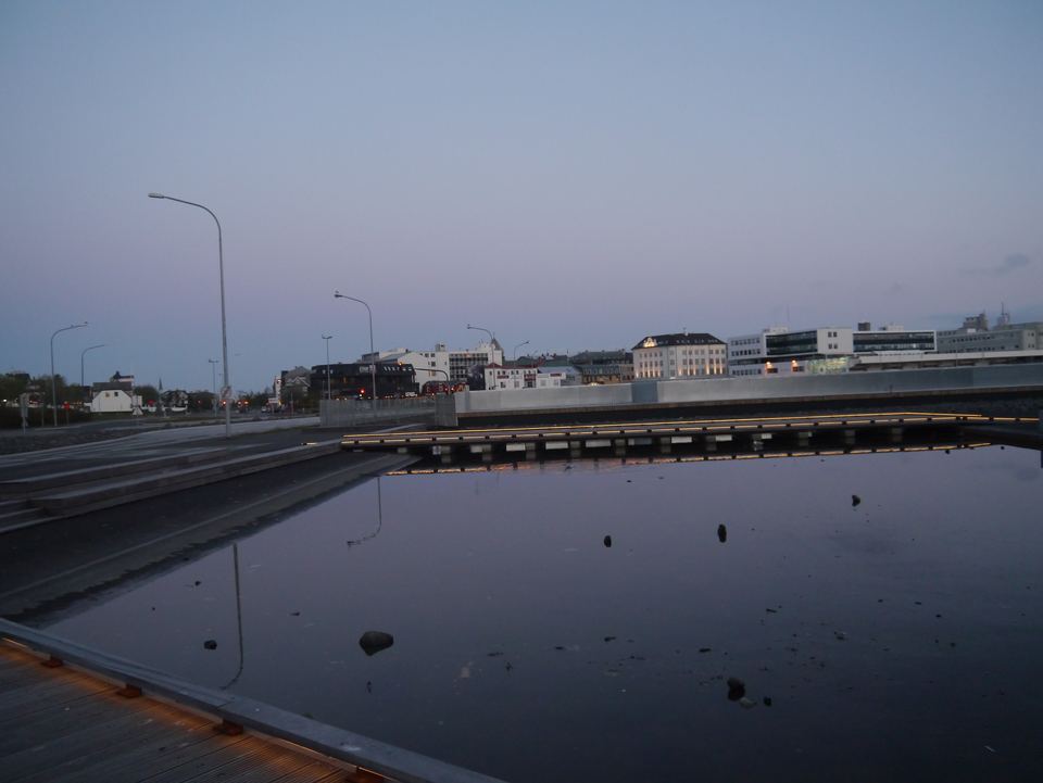 A calm pond reflecting city buildings in Reykjavík during twilight.