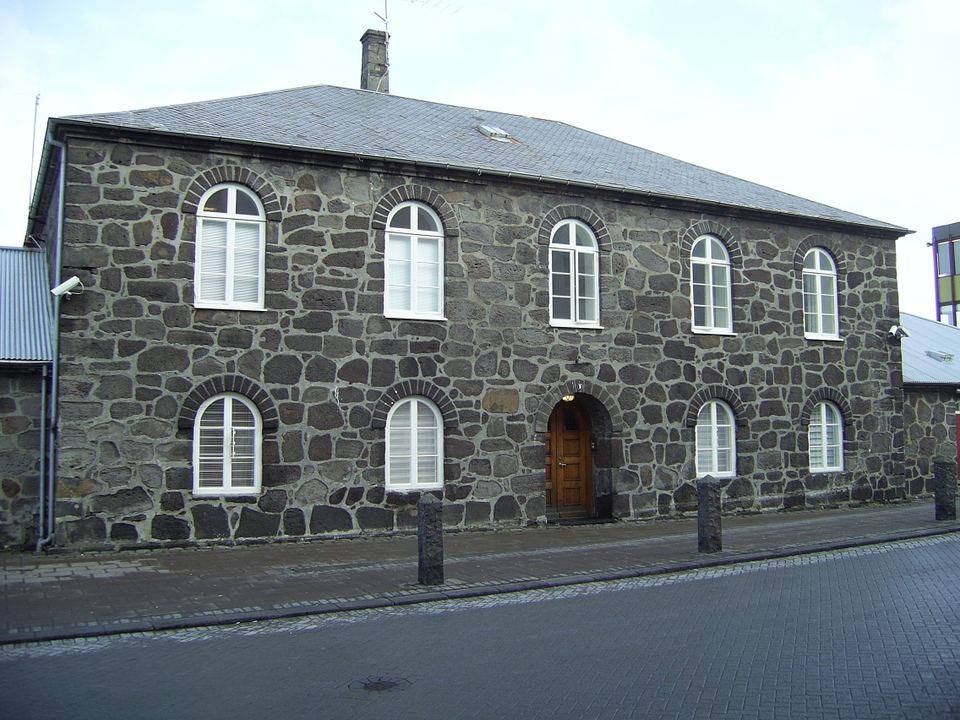 A historic stone building with arched windows along a paved street in central Reykjavik.