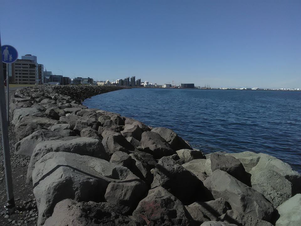 A broad waterfront lined with basalt rocks and a clear view of the distant city across the water.