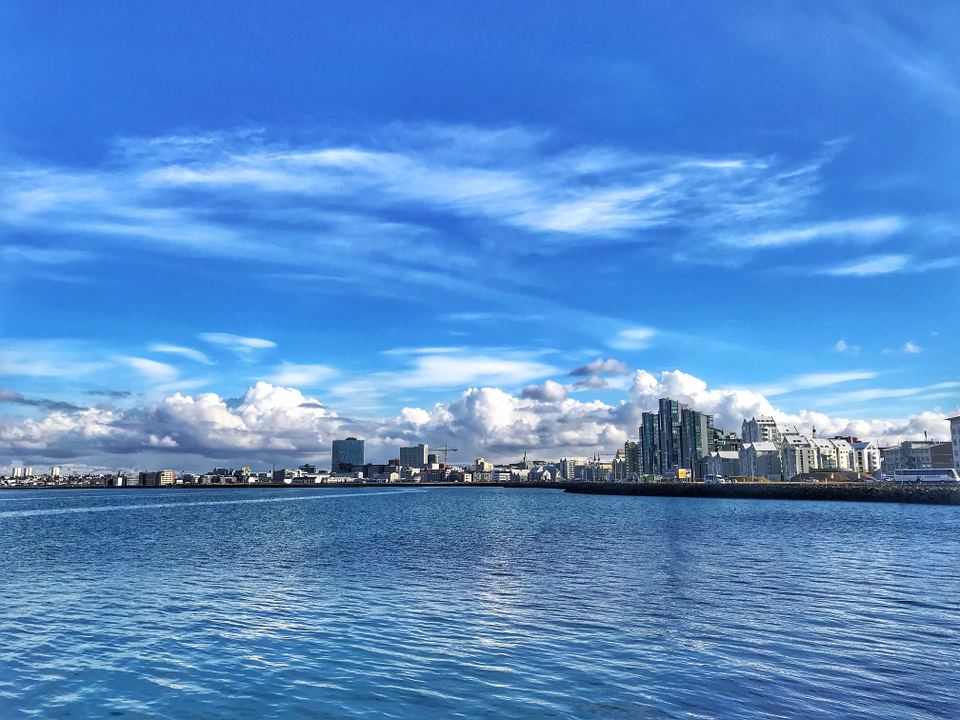 A wide waterfront view of modern buildings along the Reykjavik shoreline under a vibrant blue sky