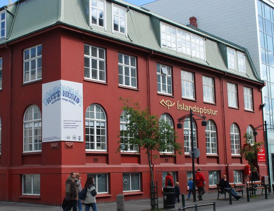 People walking on a sidewalk outside a red building in Reykjavik