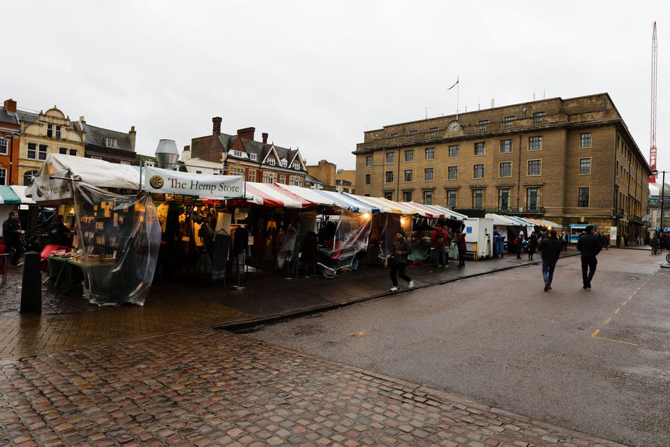 Market stalls with colorful awnings line a paved square in front of brick buildings