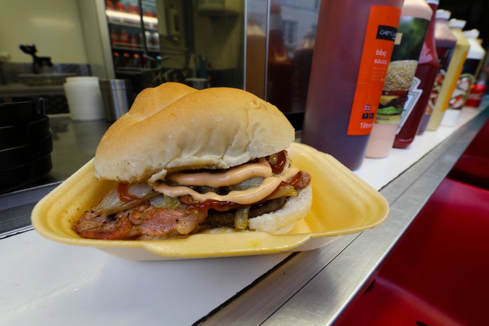 A close-up of a meat sandwich topped with sauce in a yellow foam container
