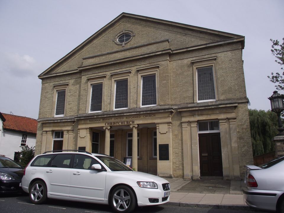 Exterior view of a brick church with stone pillars and parked cars in front.