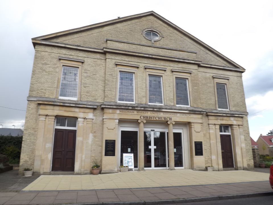 Front view of a light brick church building with columns and double glass entry doors.