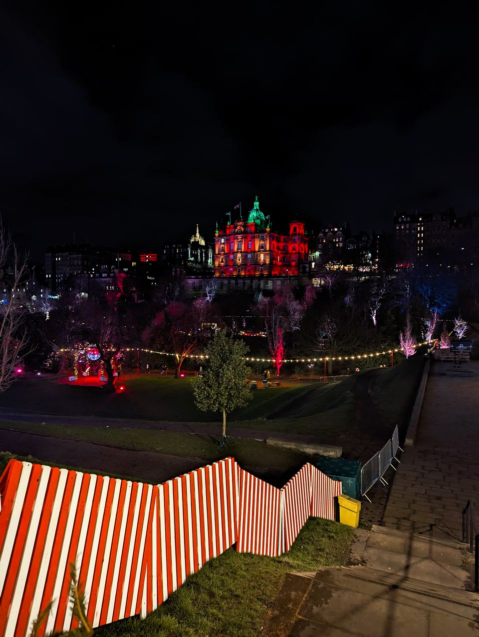 Striped barriers along a pathway leading toward illuminated historic buildings at night