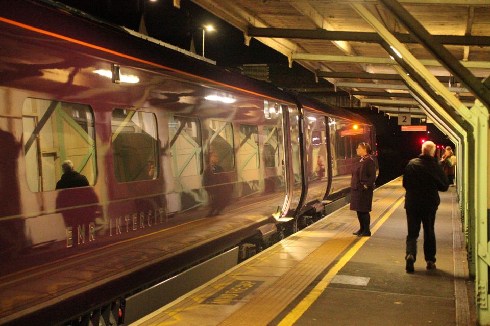Passengers standing on an illuminated station platform next to an EMR InterCity train at night