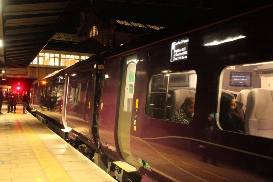 A purple passenger train stopped along a brightly lit station platform at night