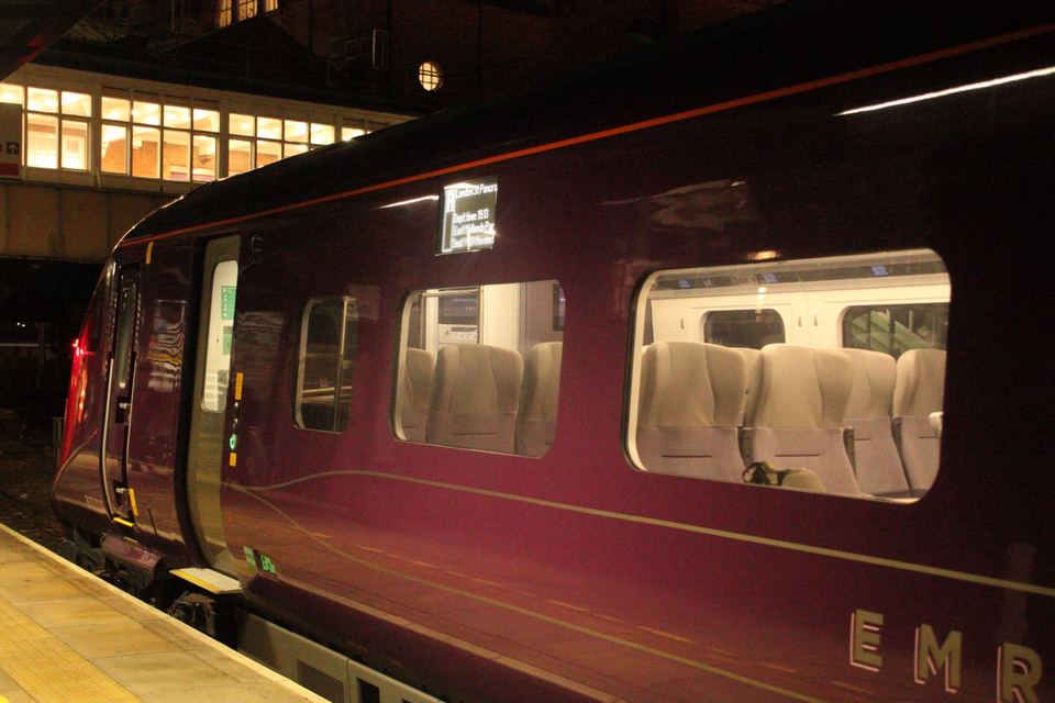 A purple passenger train stopped at a train station platform at night.
