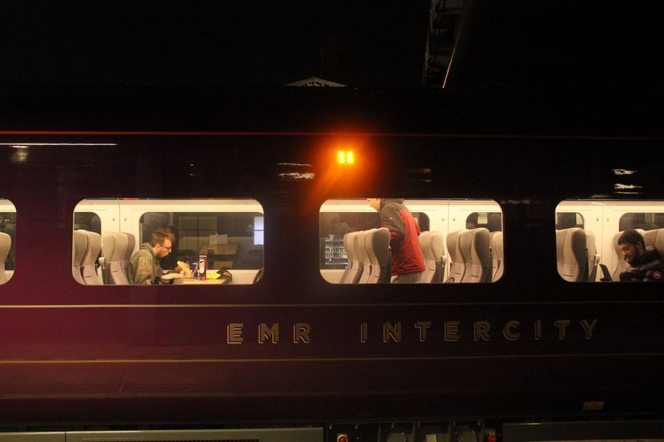 Passengers sitting inside a train carriage on an East Midlands Railway train at night.