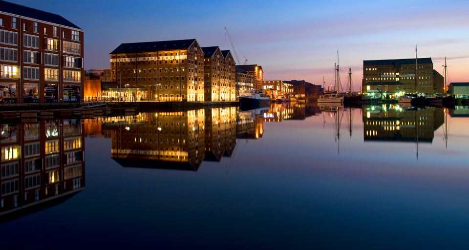 Historic brick warehouses and boats reflected in calm harbor waters at dusk