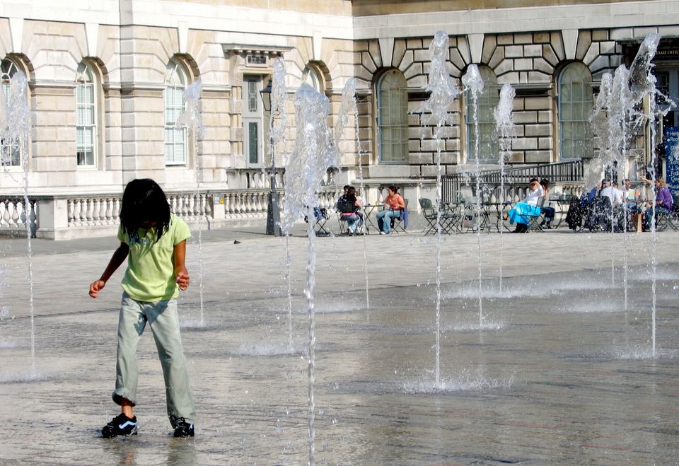 Child playing among water jet fountains in a paved courtyard