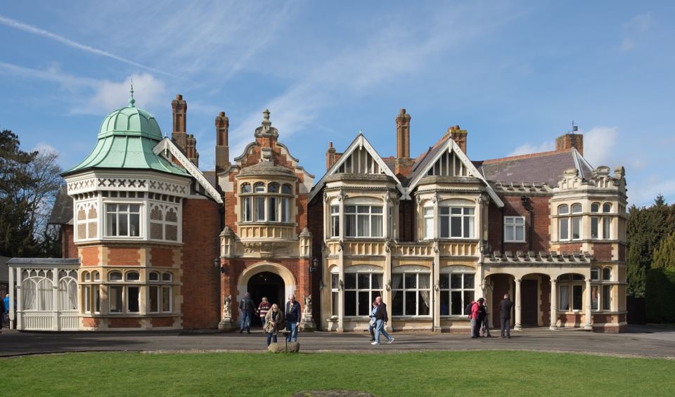 Exterior view of an ornate red brick mansion with a green dome and front lawn