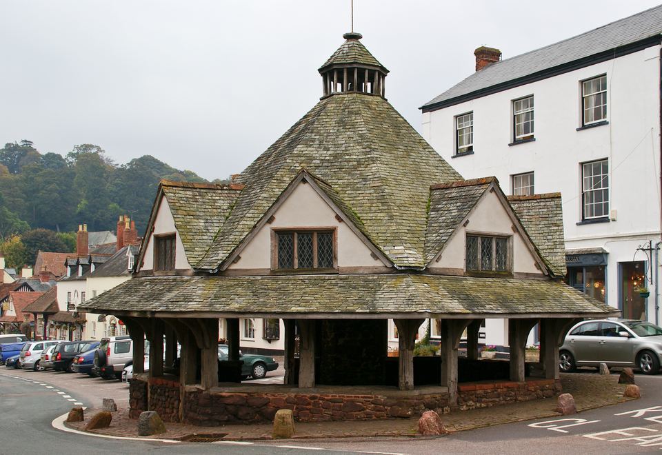 An octagonal wooden market hall with a stone base and slate roof on a village street.