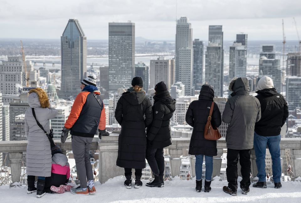People in winter clothing standing along a stone terrace overlooking city skyscrapers in winter.