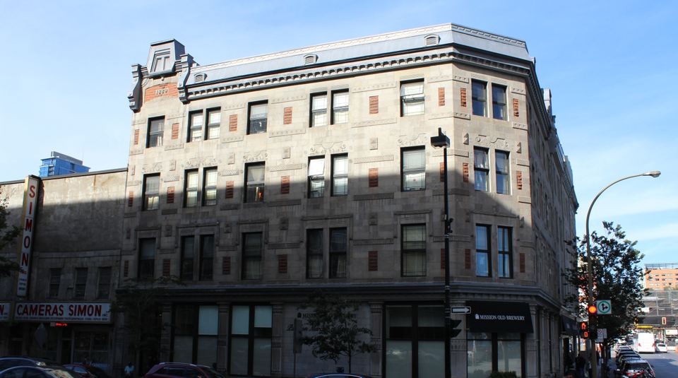 A corner view of a multi-story stone building under a blue sky.