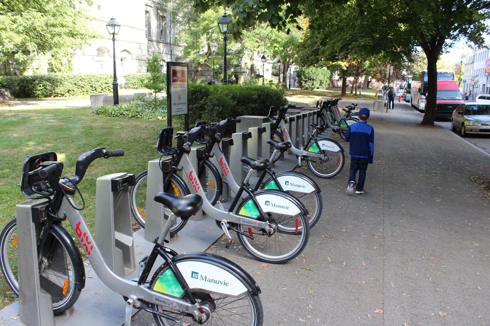 A row of public bike-share bicycles docked on a sidewalk next to trees.