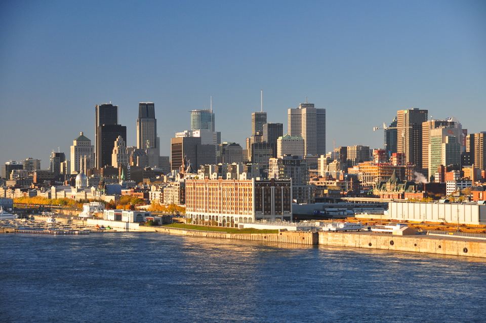 City skyline along the waterfront lit by warm sunlight across blue water.