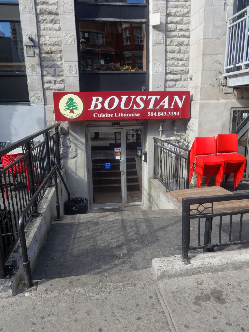 Concrete steps leading down to a restaurant entryway next to stacked red chairs.