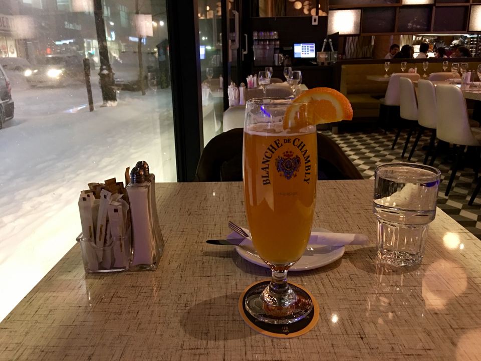A glass of beer on a dining table with a view of a snowy street through the window