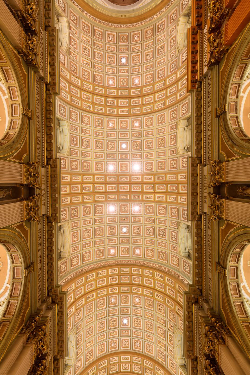 Looking straight up at a detailed gold and cream coffered vault ceiling.
