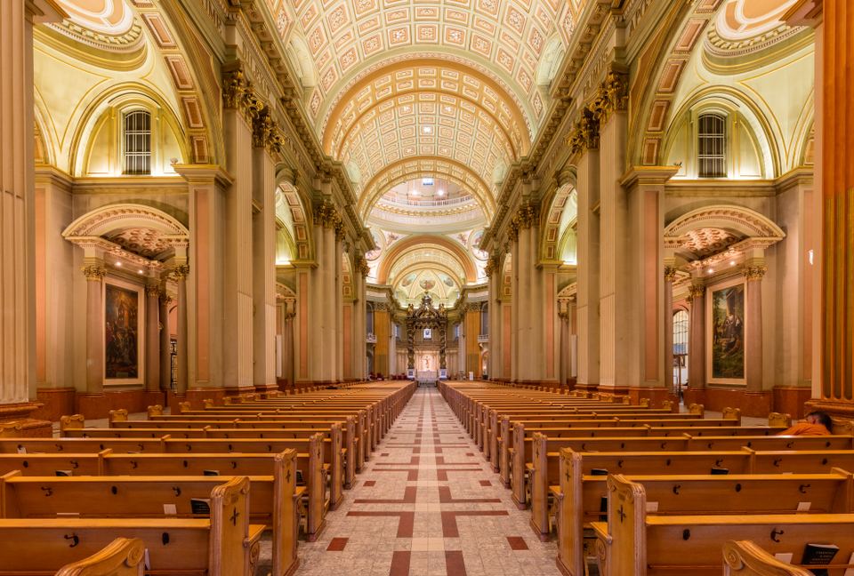 Wide interior perspective down a long church aisle lined with arches and classical columns.