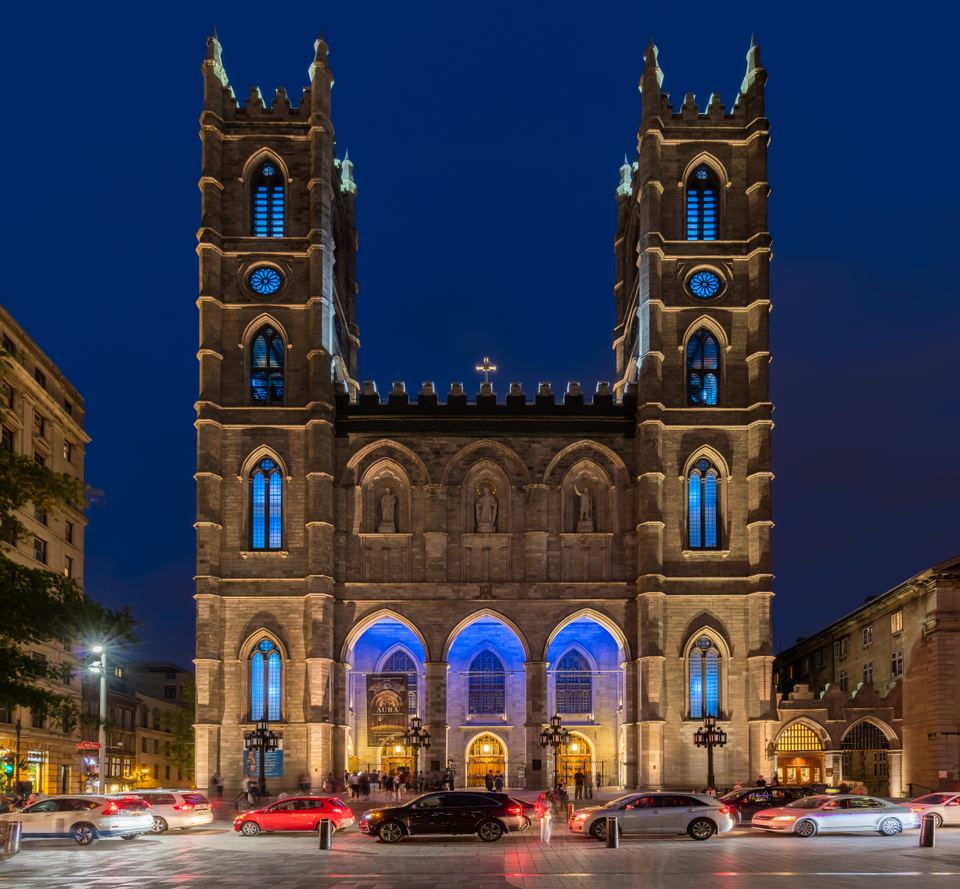 Gothic Revival cathedral front facade lit in blue and golden light against a dark blue sky.