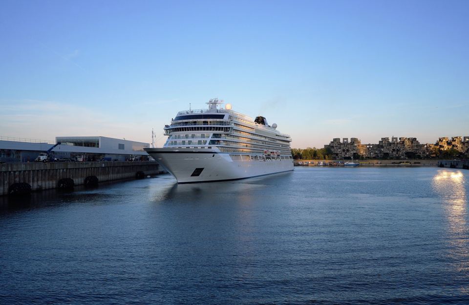 Large white cruise ship docked at the Montreal port terminal with Habitat 67 in the background