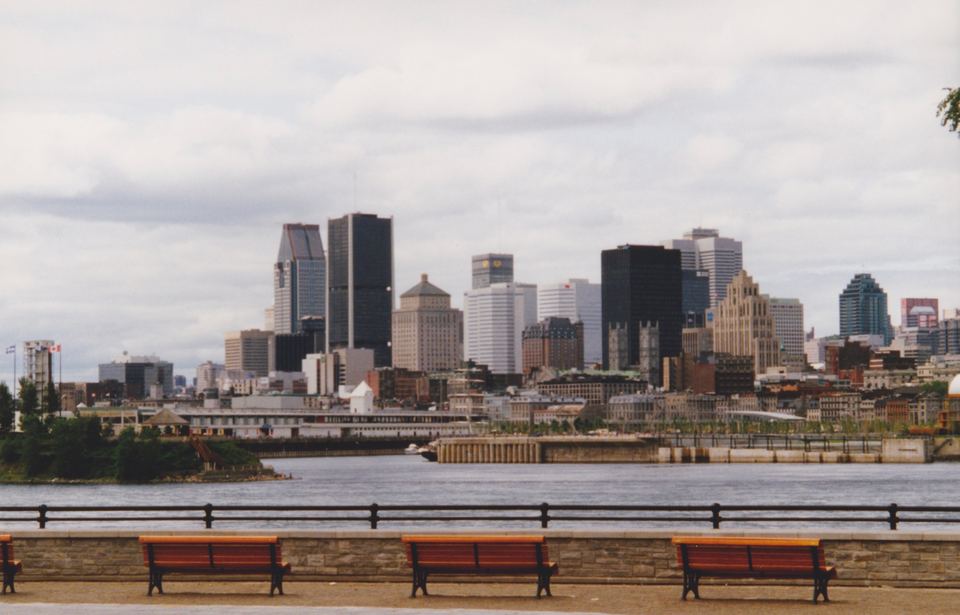 Three wooden park benches facing across water toward a distant downtown skyline