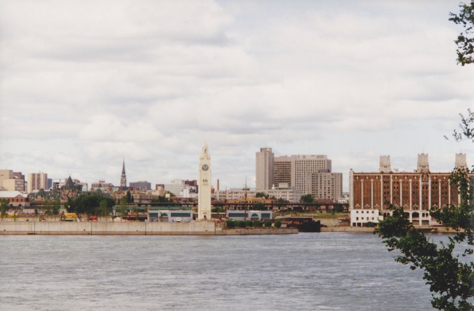 A tall white clock tower standing beside the water in front of a city skyline