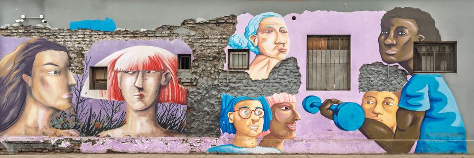 A wide building wall decorated with vibrant painted portraits of people.