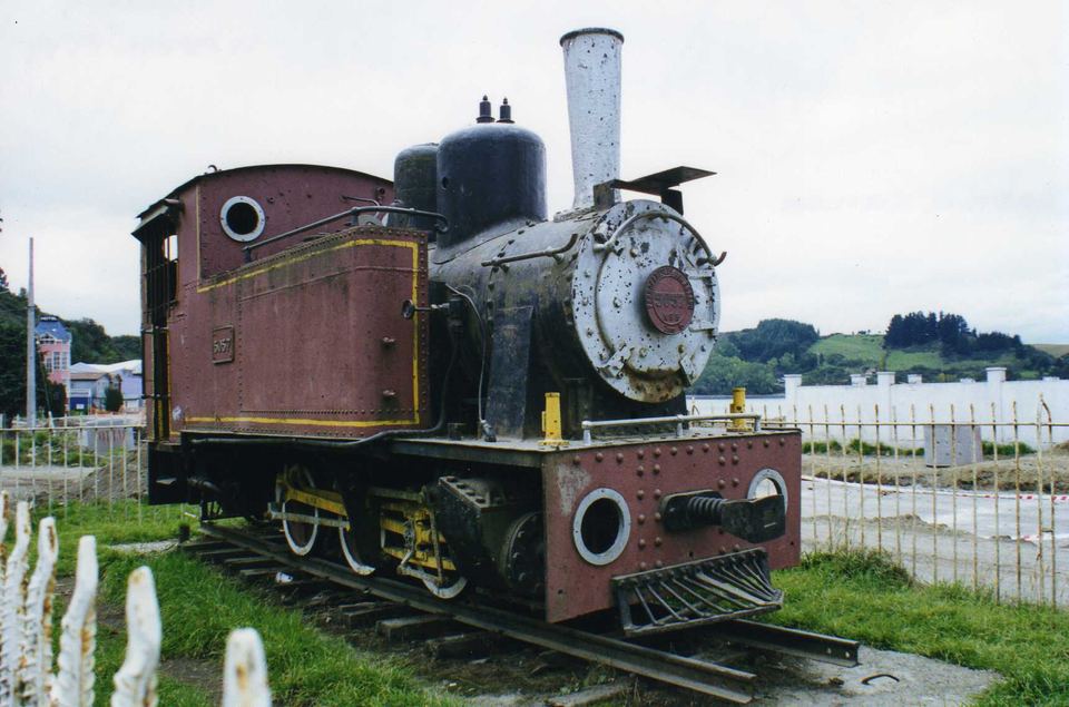 A historic steam locomotive displayed on short tracks near a fence in Chile