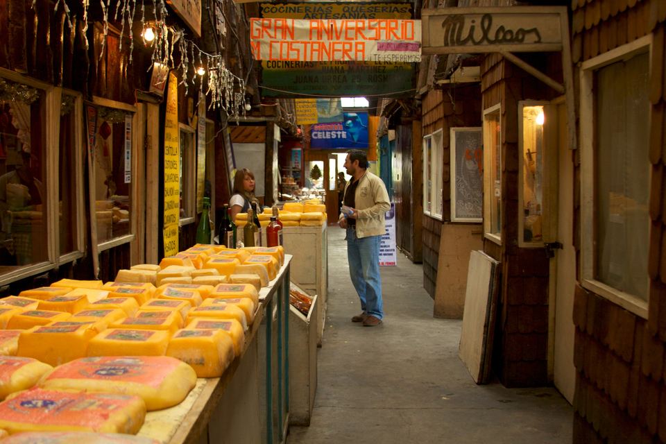 Blocks of cheese arranged on displays along a wooden market corridor in Chile.