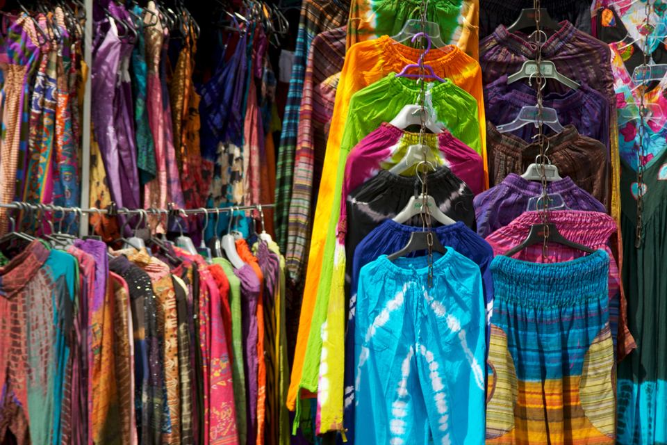 Brightly colored tie-dye clothing hanging on racks at a market stall