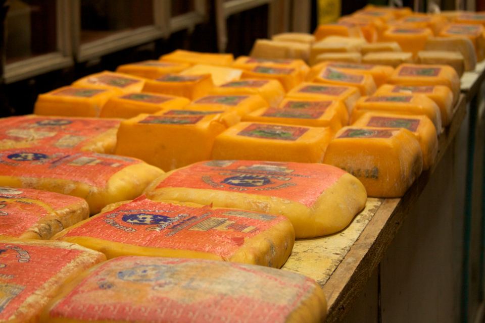 Large blocks of packaged yellow cheese arranged on a wooden counter inside a market.
