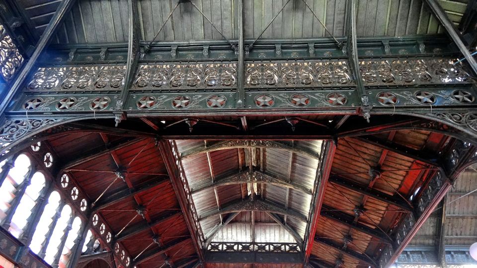 Low angle view looking up at decorative iron arches and wooden ceiling beams.