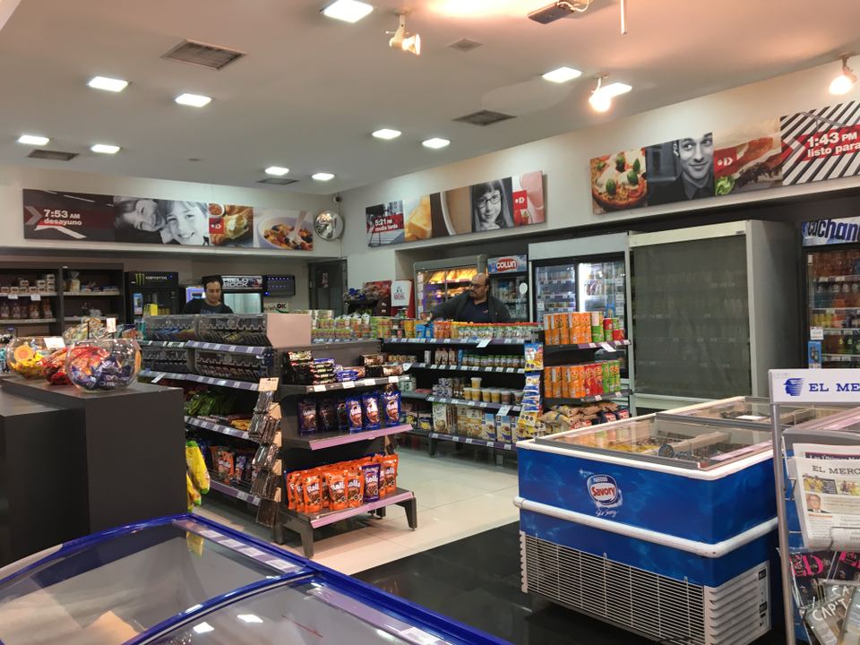 Interior of a brightly lit Chilean convenience store with shelves of snacks and ice cream freezers.