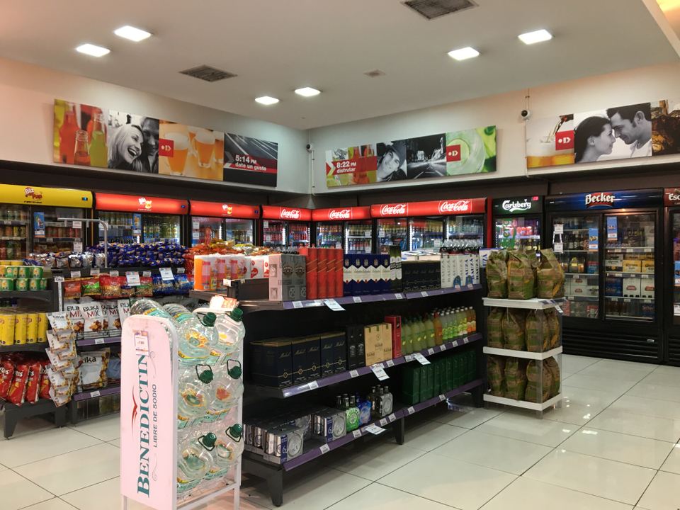 Inside view of a brightly lit convenience store with shelves of drinks and snacks.