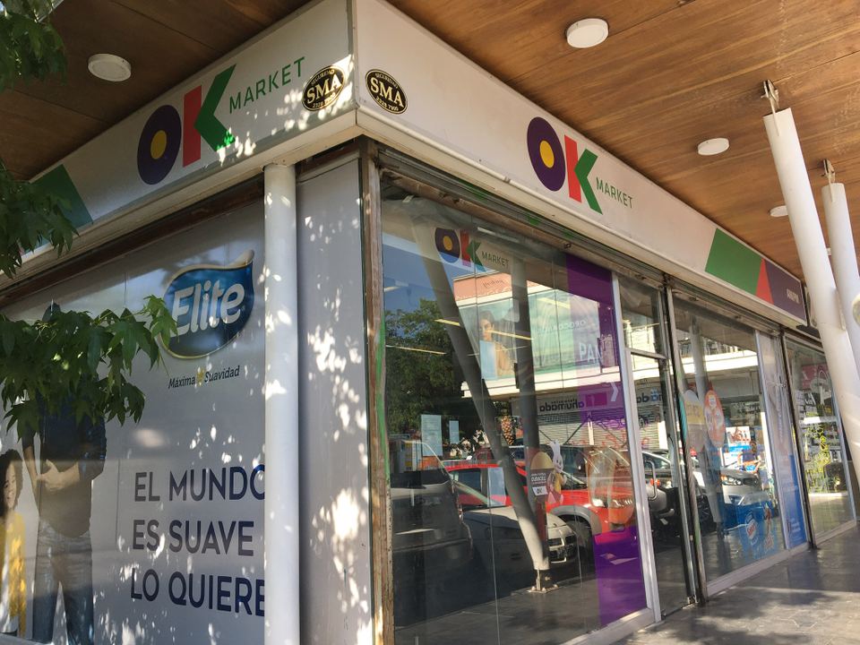 Glass storefront of a Chilean convenience store under a covered walkway.