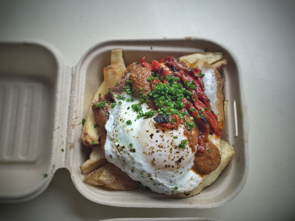Takeaway container filled with fries, meat, roasted peppers, and a fried egg