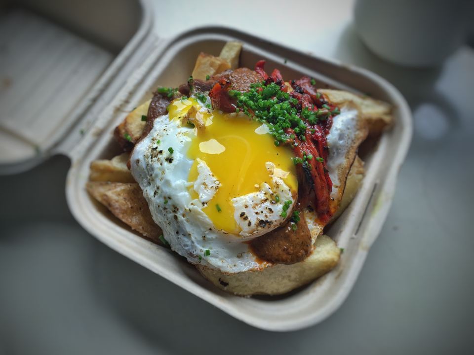 Loaded fried potatoes topped with a sunny-side-up egg in a takeaway container