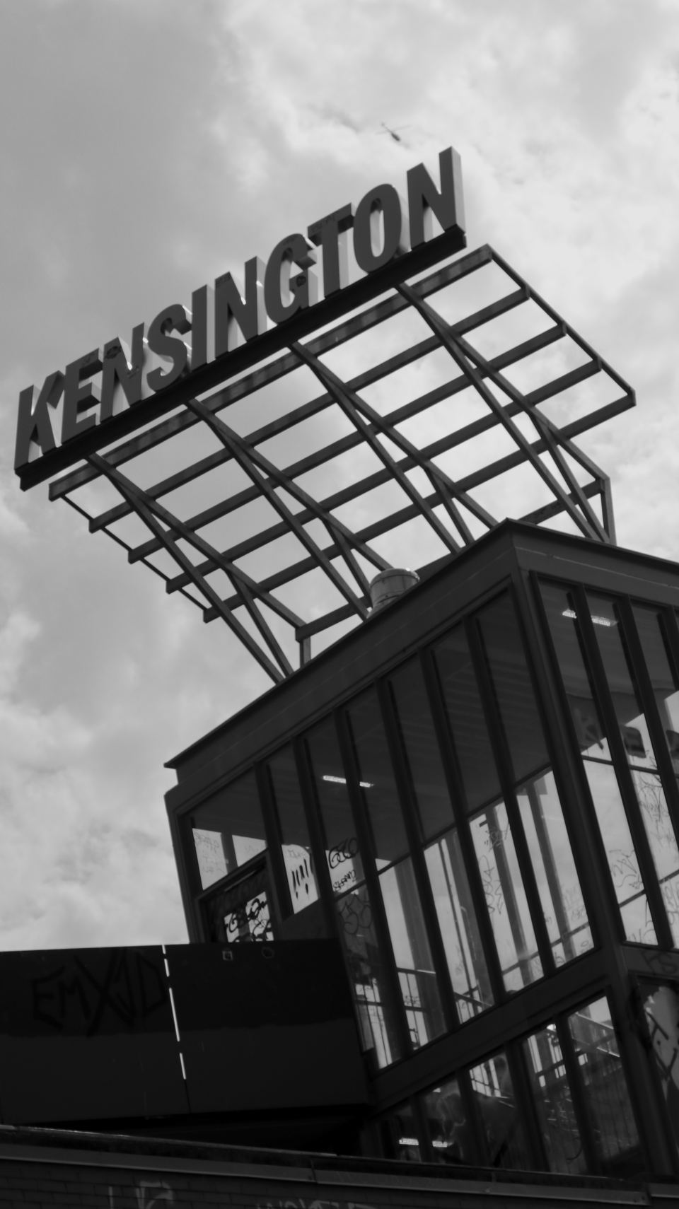 Black and white photograph looking up at a tall metal Kensington sign structure