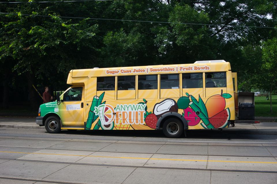 A yellow food truck decorated with fruit graphics parked beside streetcar tracks.