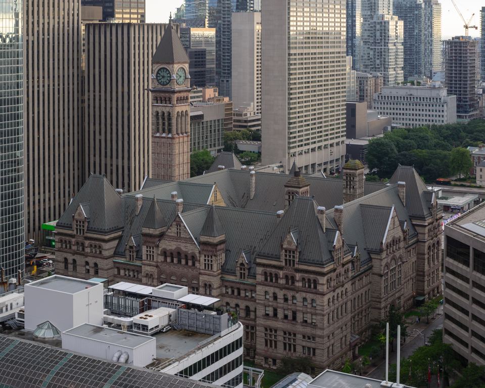 High-angle view of a historic stone building with a clock tower nestled among modern skyscrapers.