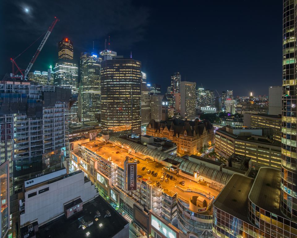 A high-angle night skyline photograph of illuminated high-rises and historic architecture in downtown Toronto.